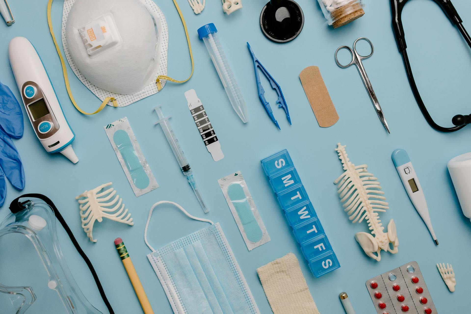 Flat lay of medical supplies: PPE, diagnostics, instruments, and anatomical models on a clinical blue background