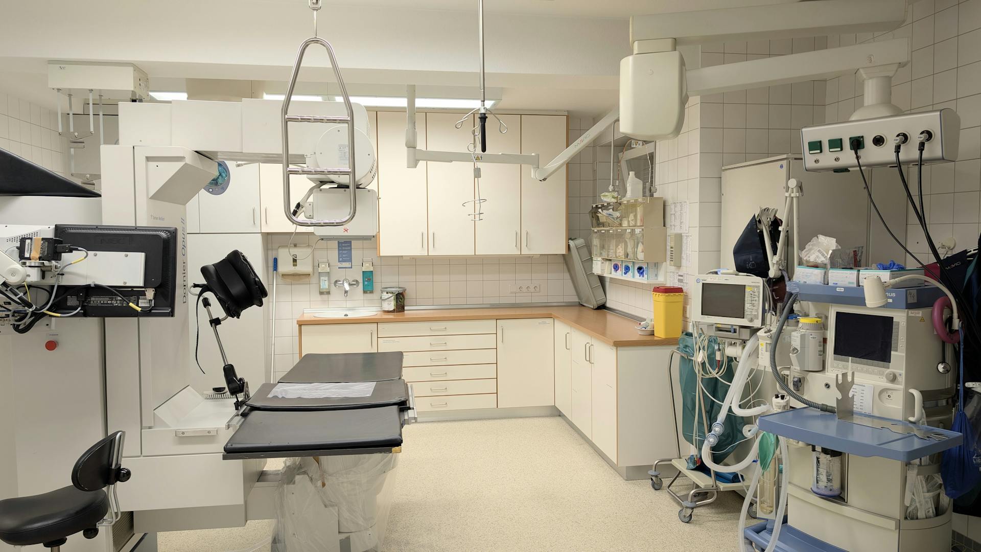 Modern clinical procedure room with examination table, surgical equipment, and monitors